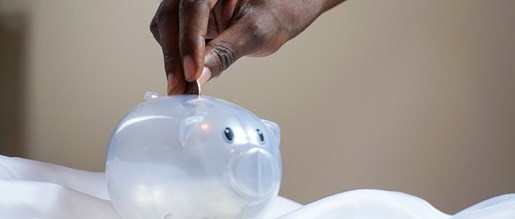 A person slotting coins into a clear piggy bank
