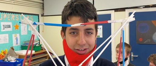 A student proudly showing off a bridge they made from straws and other materials