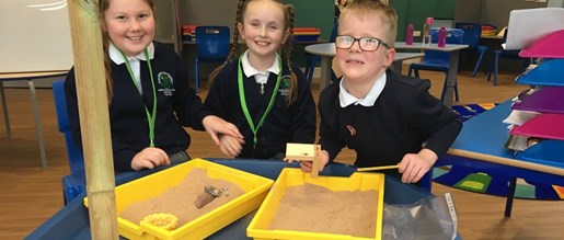 Three children proudly showing off the rocks they found in their sand trays
